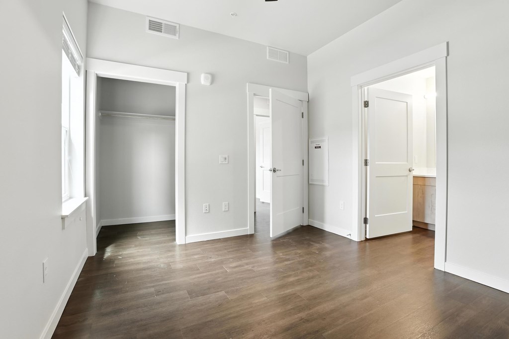 A room with white walls and wooden flooring, with a door on the left and a door on the right.