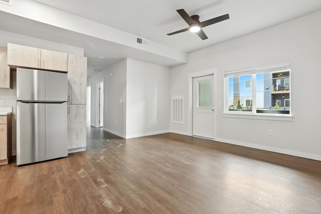 A spacious kitchen with a refrigerator, wooden floors, and a ceiling fan.