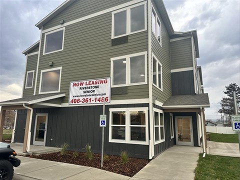 A two-story building with a sign that says "NOW LEASING" and a website address.
