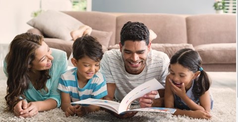 A family of four is lying on the floor and reading a book together.