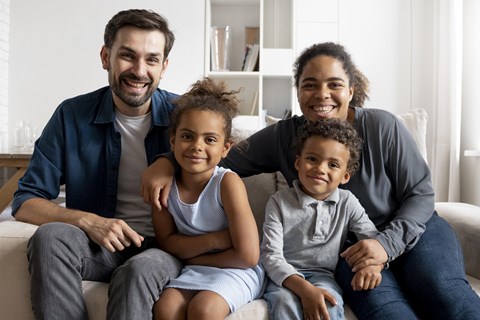 A family of four is sitting together on a couch.