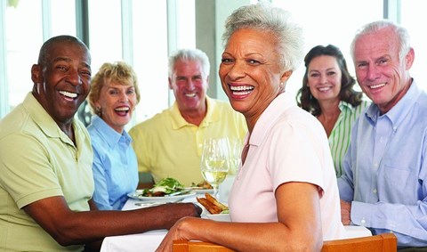 A group of people are sitting around a table smiling and enjoying a meal together.