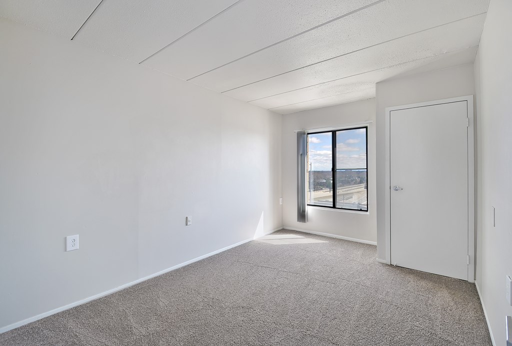 A room with a carpeted floor and a window with a view of the outside.
