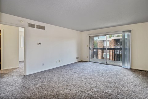 A spacious room with a grey carpet and a sliding glass door leading to a balcony.