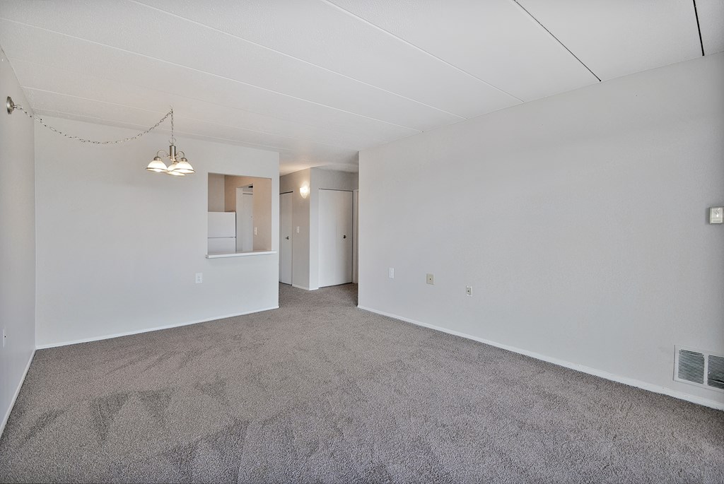 A large empty room with a carpeted floor and a hanging light fixture.