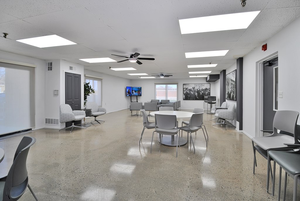 A room with a white ceiling and a grey floor with chairs and tables.