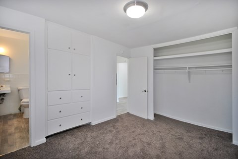 A white bedroom with a closet and a toilet visible in the bathroom.