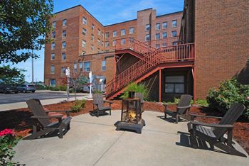 a patio with rocking chairs and a fire pit in front of a brick building