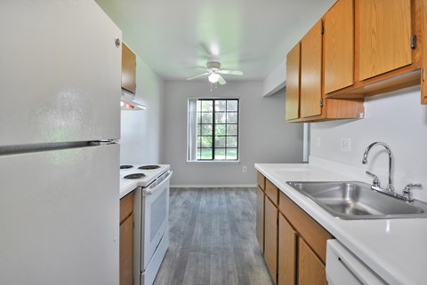 A kitchen with a white fridge, wooden cabinets, and a window.