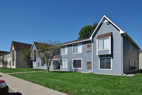A grey house with a red car parked in front.