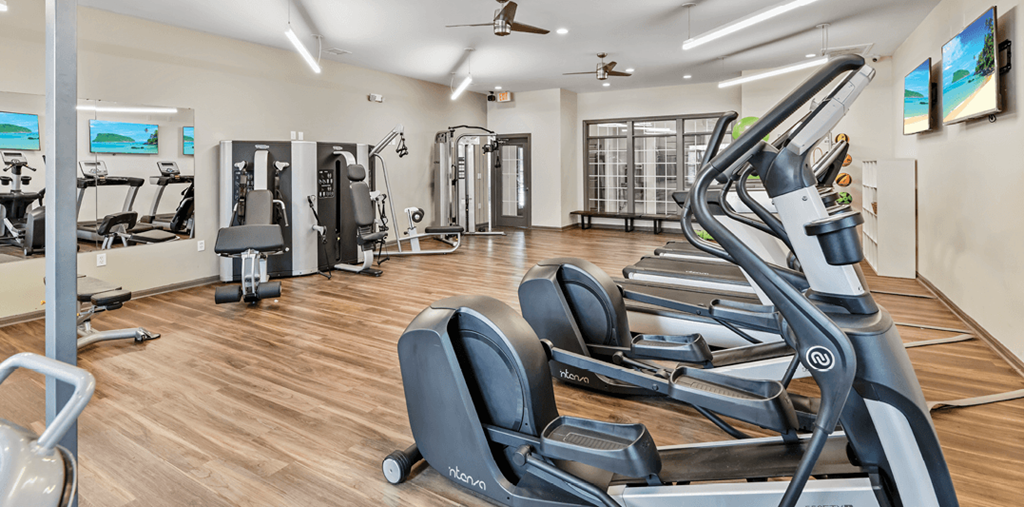 a gym with cardio equipment and weights on a wood floor