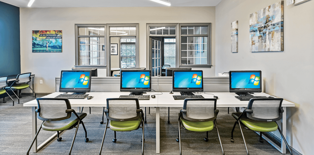a long table with laptops and chairs in a room with windows