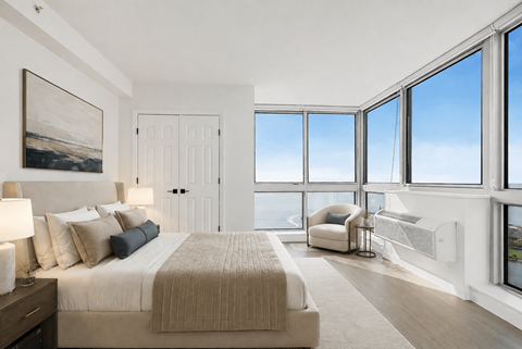 A bedroom with a large bed and a view of the sky through the windows.