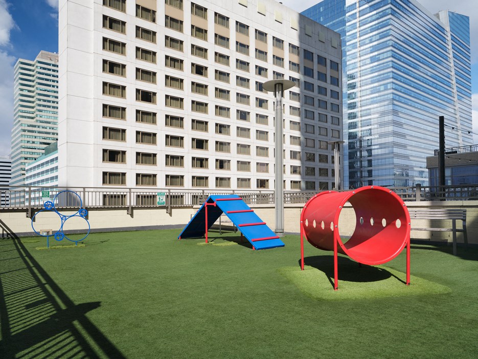 A playground with a red tunnel and slide on a green lawn in front of a white building.
