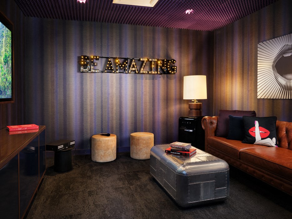A room with a brown couch and a sign that says "Be Amazing" on the wall.