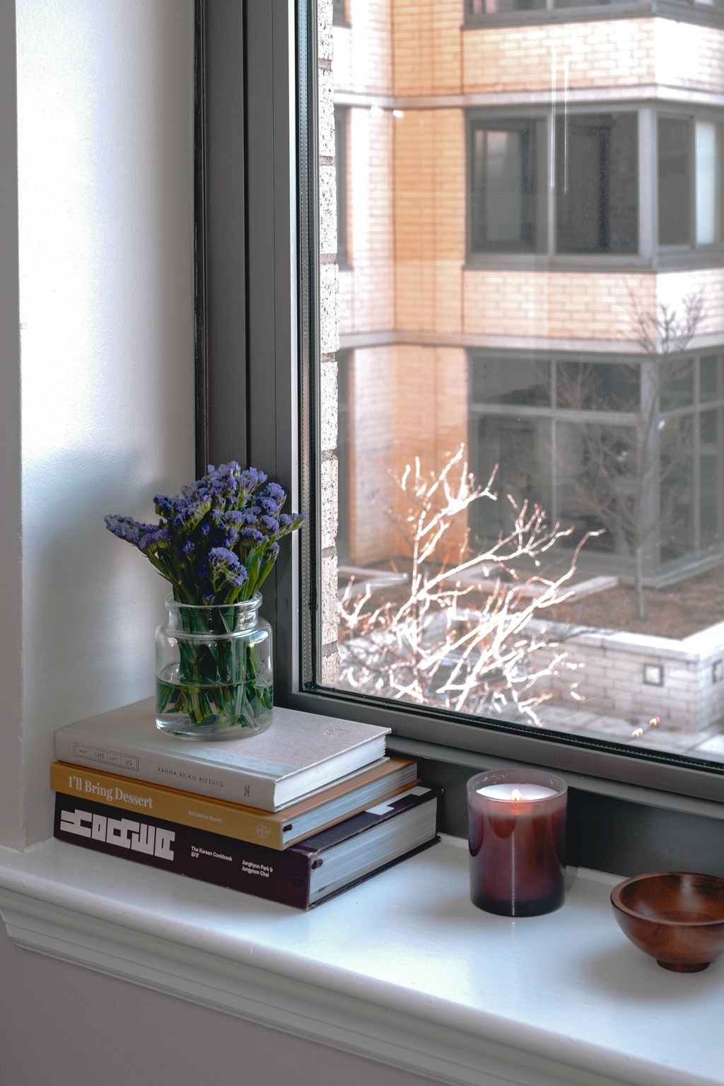 A candle, a book, and a vase with flowers are on a windowsill.
