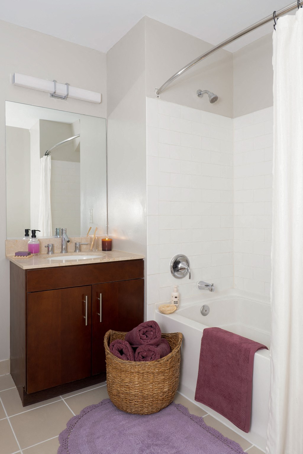A white bathroom with a purple rug and a basket of towels.