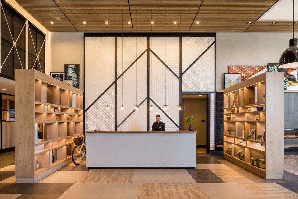 a man stands at a desk in a lobby with a white counter and shelving