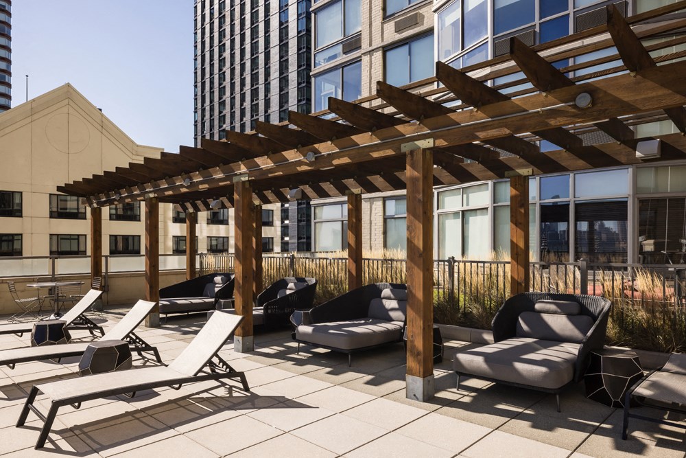 A wooden pergola provides shade for lounge chairs on a rooftop patio.