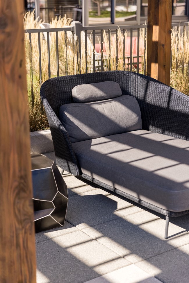 a black wicker lounge chair with cushions on a patio