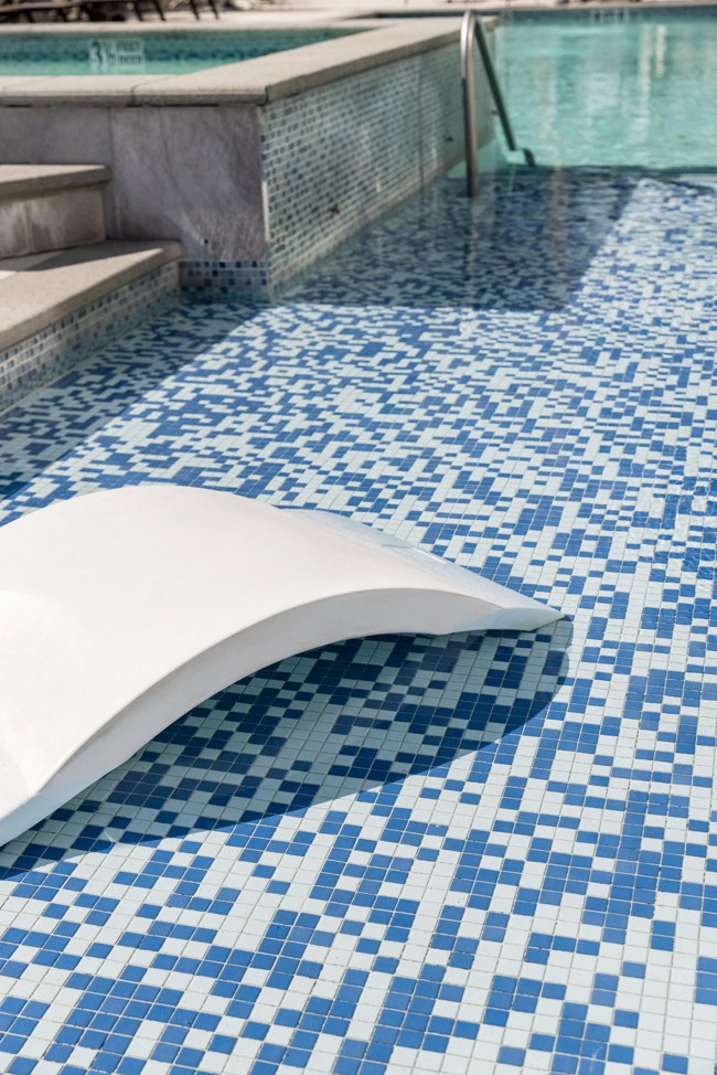 a swimming pool with blue tile flooring and a white bench