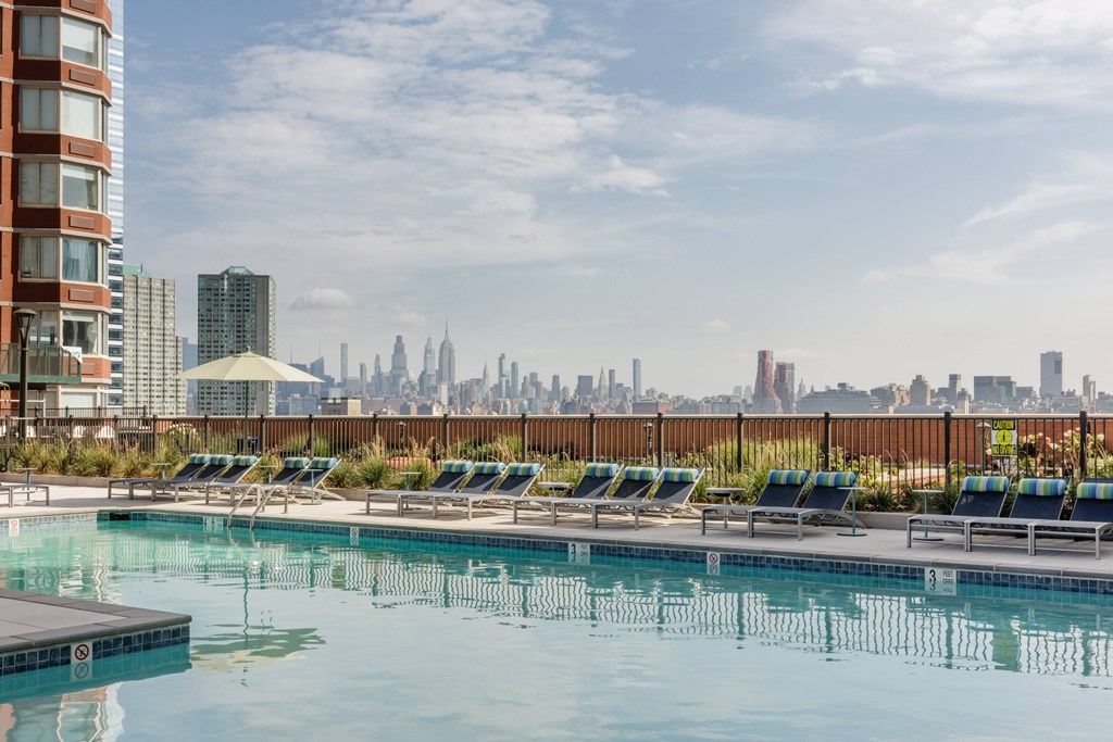 A pool with lounge chairs and a city skyline in the background.