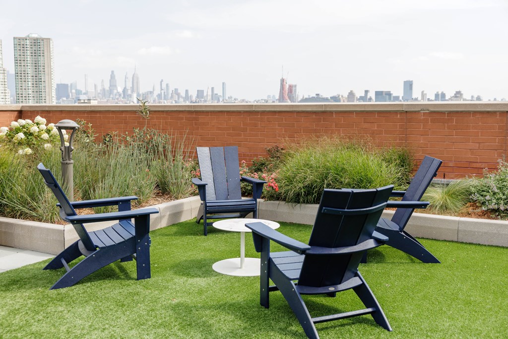 A set of outdoor furniture including chairs and a table is set up on a grassy area with a city skyline in the background.