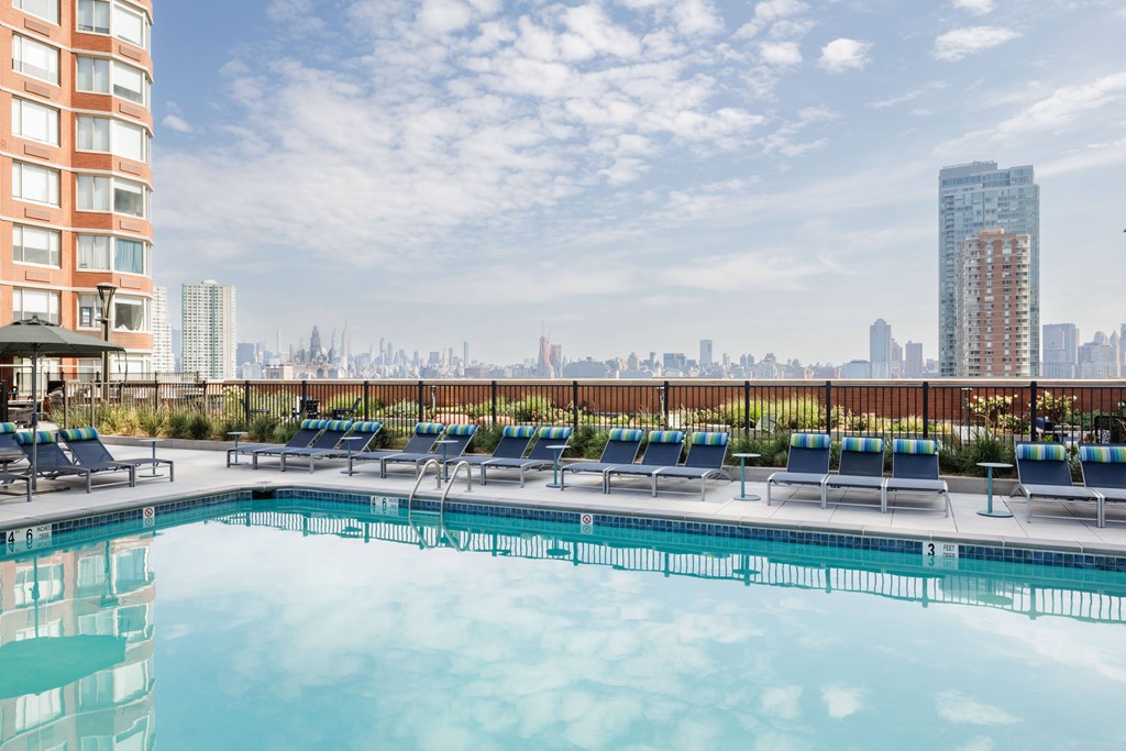 A swimming pool with lounge chairs and a city skyline in the background.