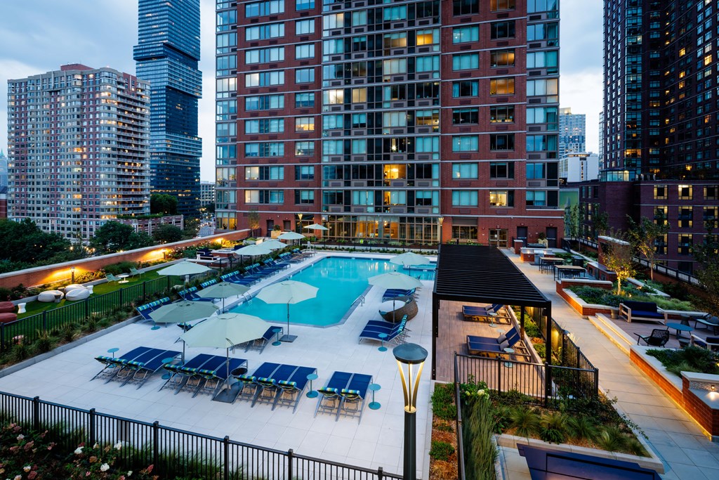 A large swimming pool surrounded by a black fence and several lounge chairs.