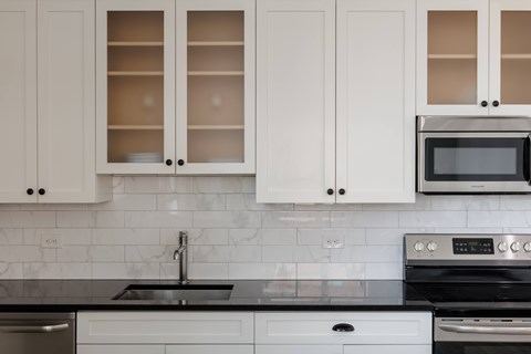 A kitchen with white cabinets and black countertops.