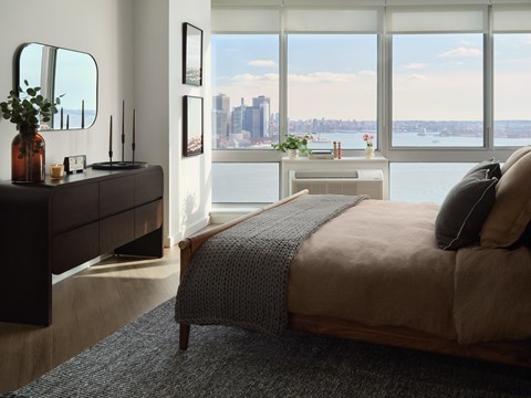 A bedroom with a large bed and a city view through the window.