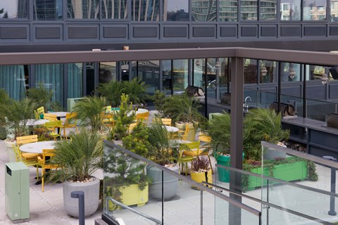 A glass railing separates the outdoor seating area from the building behind it.