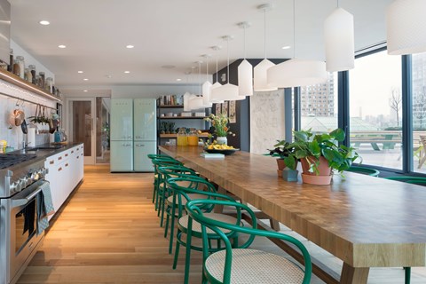 A long wooden table with green chairs is in the middle of a kitchen.