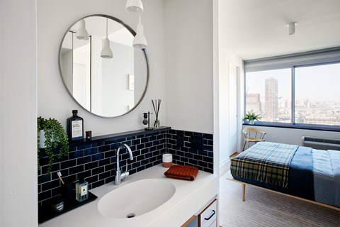 A bathroom with a round mirror and a window overlooking a cityscape.