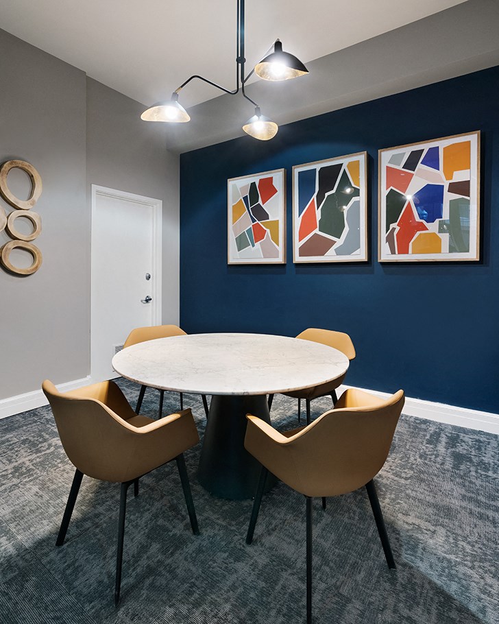a round table with four chairs in a room with a blue wall and paintings