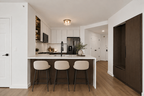 A kitchen with white cabinets and a white island with three bar stools.