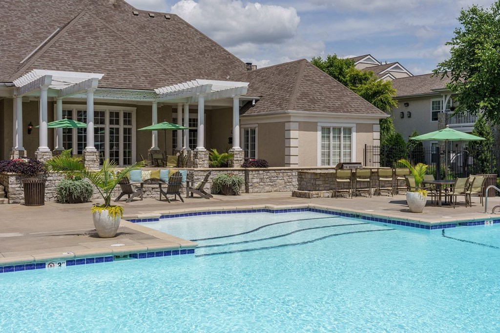 a swimming pool with chairs and umbrellas in front of a house
