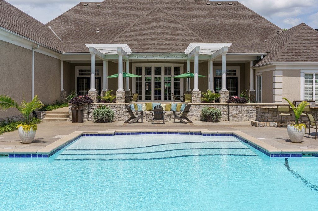 a swimming pool in front of a house with chairs and umbrellas