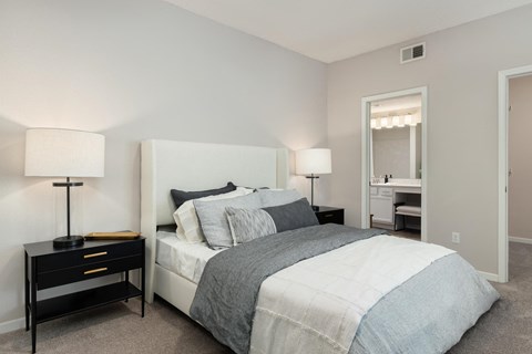 a bedroom with a bed and two nightstands and a bathroom with a mirror