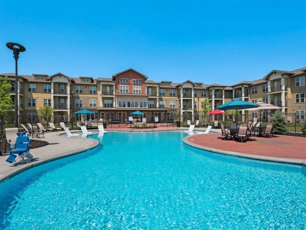 a large pool with chairs and umbrellas in front of an apartment building