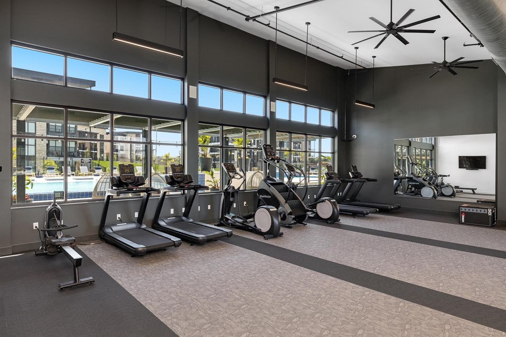 a gym with cardio equipment and windows with a pool