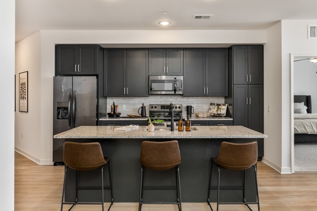 kitchen with black cabinets and a granite island with three stools