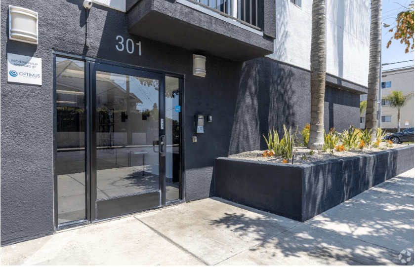 the front of a building with glass doors and a sidewalk