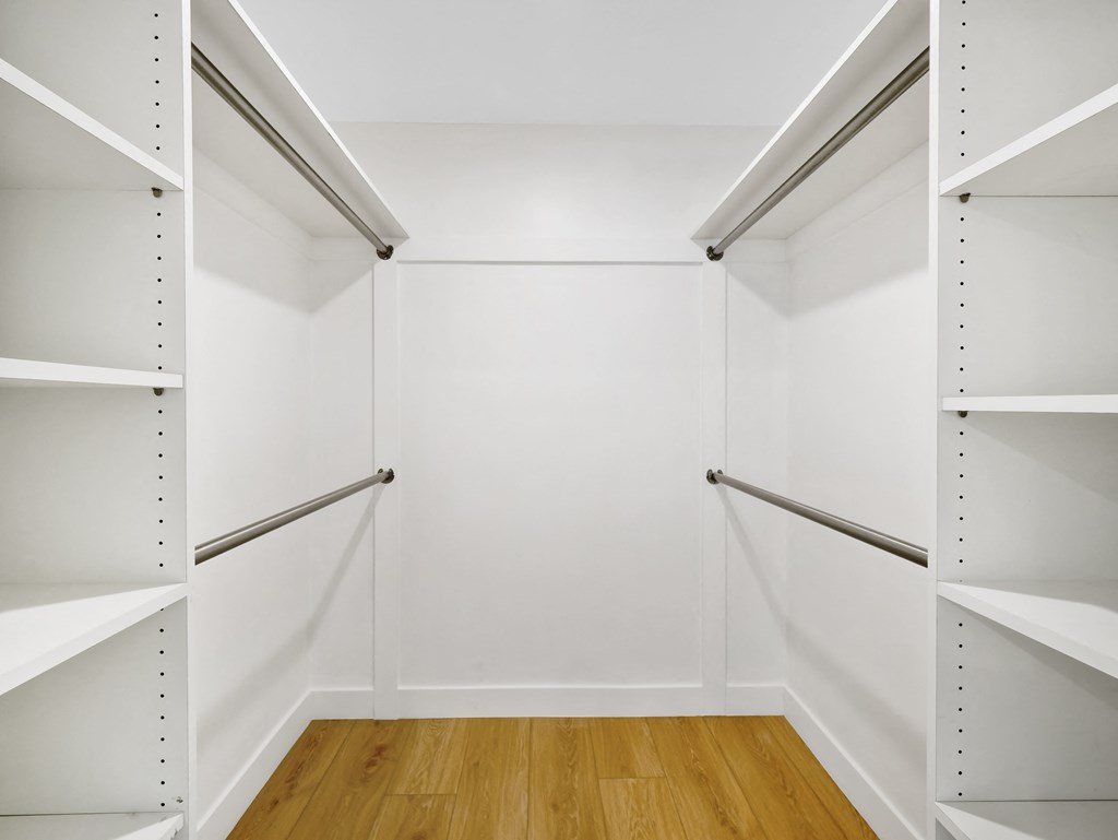 a walk in closet with white walls and wooden floors