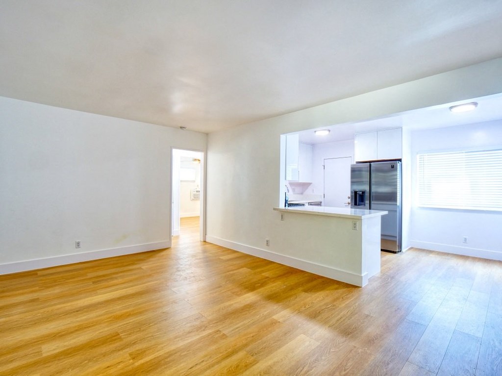 the living room and kitchen of an empty apartment with wood flooring and white walls
