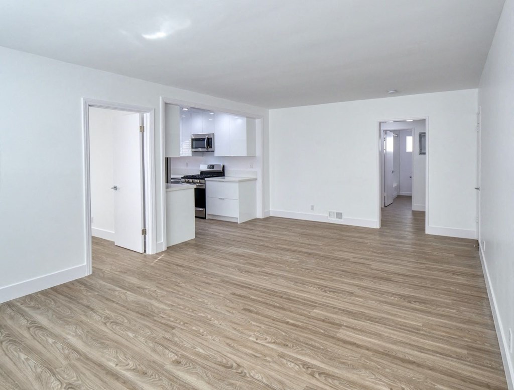 a living room and kitchen with white walls and wood flooring