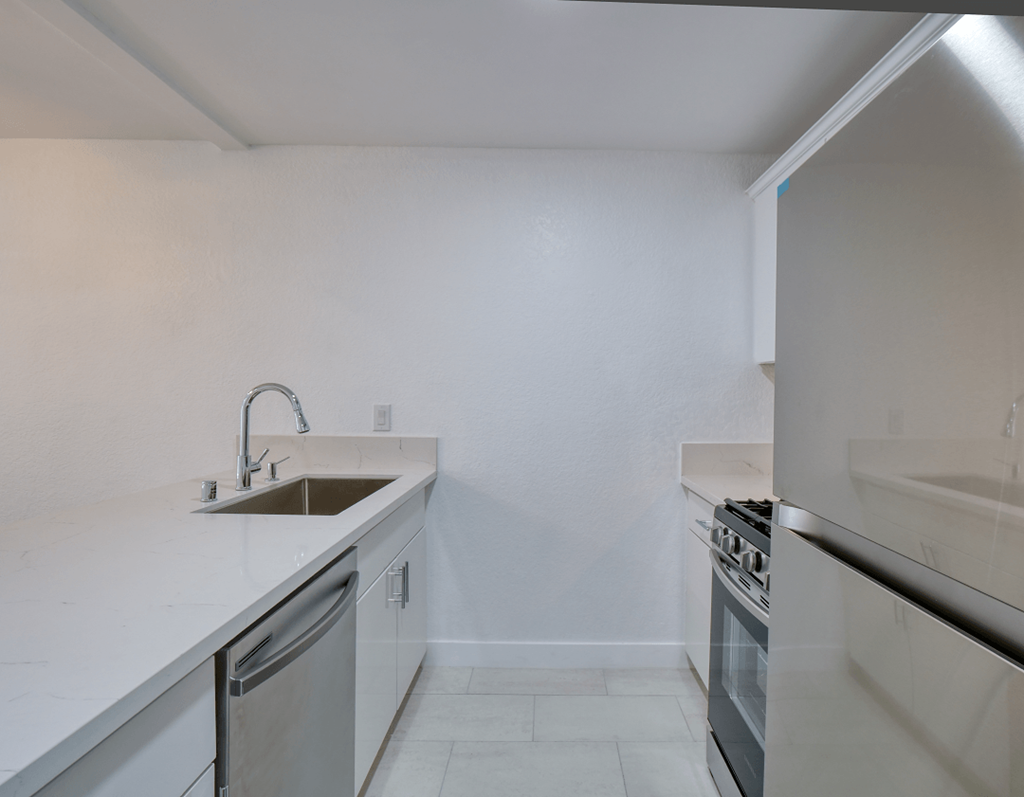 an empty kitchen with white countertops and stainless steel appliances
