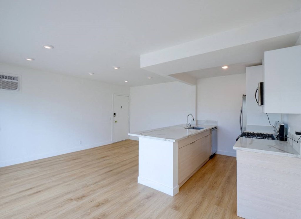 an open kitchen and living room with white walls and wood floors