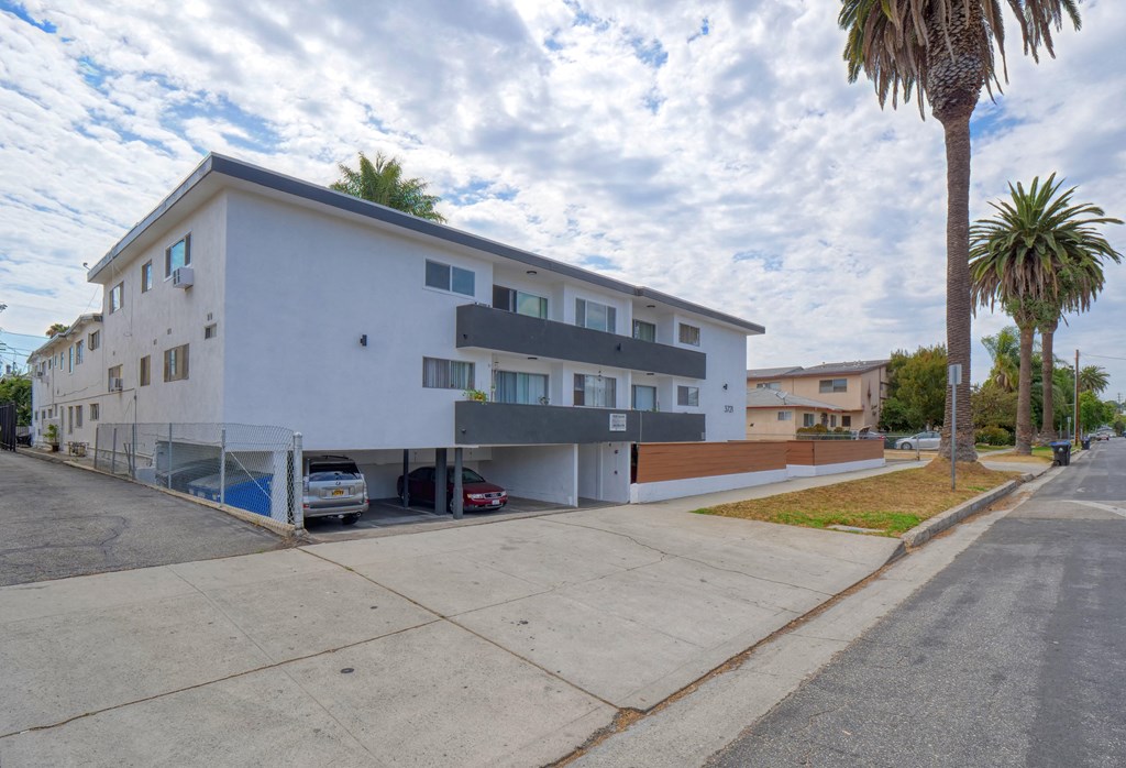 a white apartment building with a parking lot and palm trees
