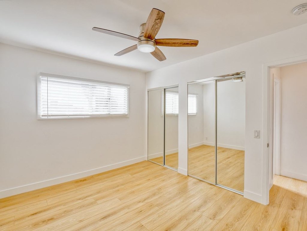 an empty bedroom with a ceiling fan and mirrored closet